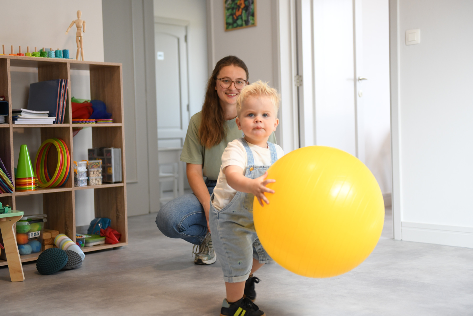 Een therapeute voert met een kind op de mat een oefening uit voor de beweeglijkheid van het been.
